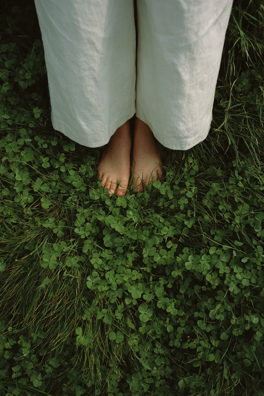 Bare feet in white linen trousers standing in thick clover and grass